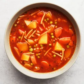 Foto van een kom simpele tomatensoep met wortel en doperwten